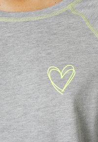 Grijze T-shirt met korte mouwen en een zachte textuur, voorzien van een neongele hartontwerp aan de voorkant en een contrasterende gestikte halslijn.