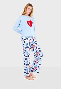 Sudadera de color azul claro con decoración de corazón rojo y pantalones de pijama de lunares azules con acentos rojos y marinos, corte relajado y textura suave.