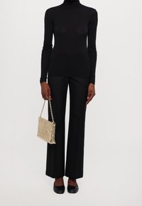 Svart långärmad polotröja med genomskinlig effekt, kombinerad med svarta vida byxor. En guldfärgad metallisk kvällsväska med kedjestropp.