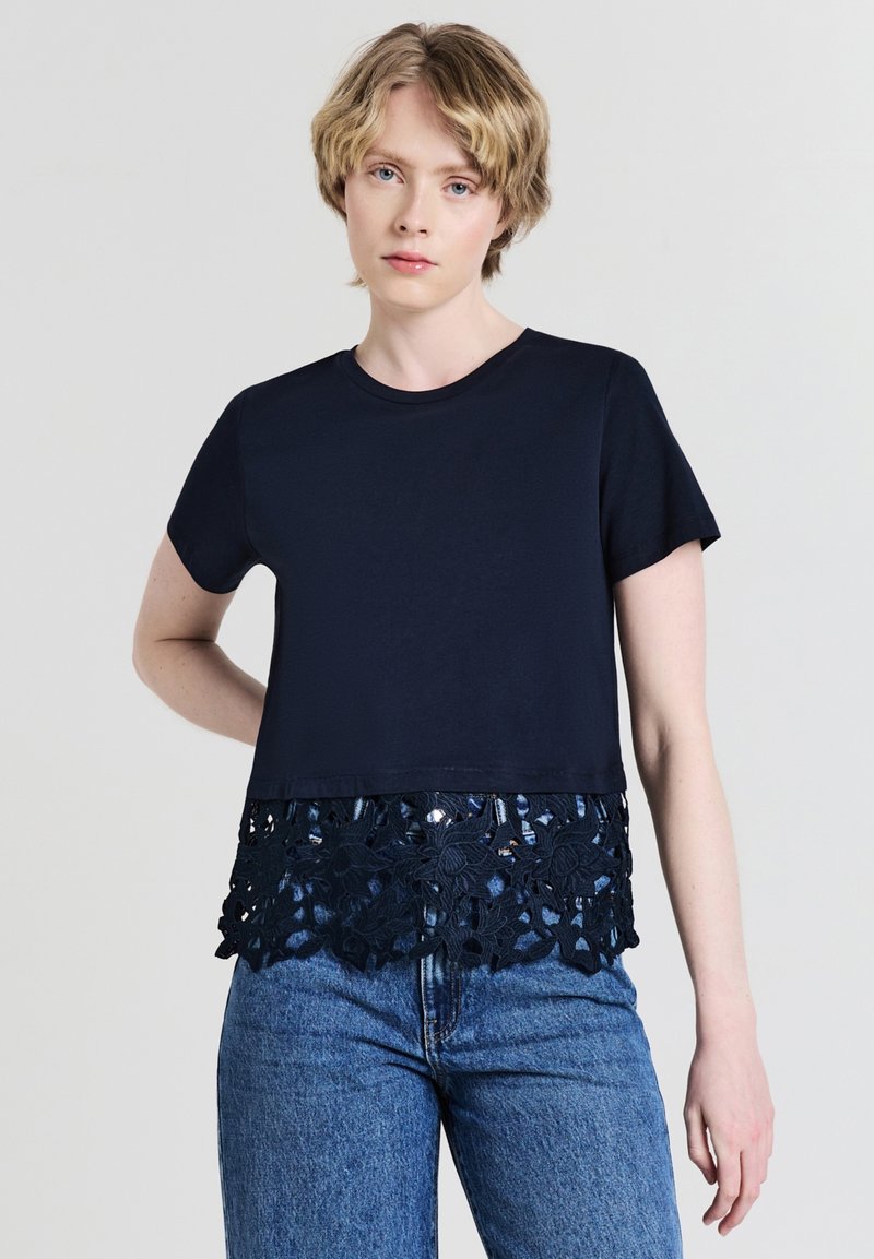 Top navy a maniche corte con orlo in pizzo che presenta motivi floreali; tessuto in cotone; vestibilità rilassata; abbinato a jeans azzurri chiari.