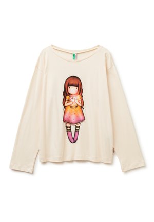 Krémová košile s dlouhým rukávem, na které je grafika bezobličí dívky v oranžovo-růžových šatech, jak drží sklenici, a má na sobě pruhované ponožky a růžové boty.