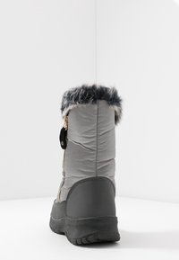 Bota gris impermeable con un puño de pelaje suave, cremallera lateral, parte superior de textil acolchado y suela de goma con un patrón de agarre texturizado.
