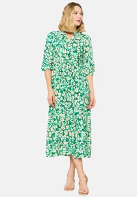 Abito maxi floreale verde con scollatura a V, maniche a tre quarti e vita arricciata. Presenta un mix di motivi astratti verdi e beige.