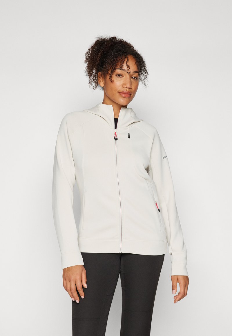 Hoodie zippé beige clair en matériau doux, avec un design ajusté, deux poches avant, des accents de fermeture éclair contrastants et une capuche.