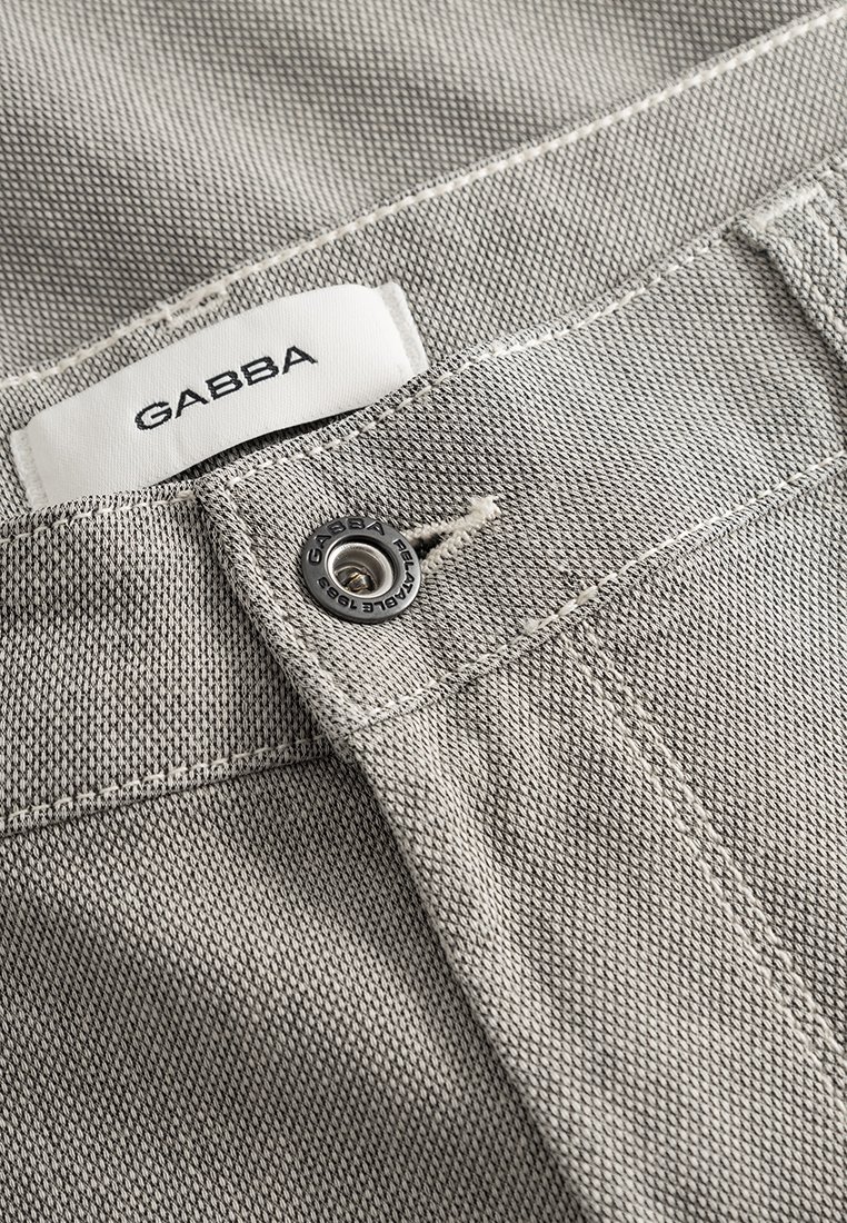 Helle graue Denim-Stoff mit glatter Textur. Verfügt über ein GABBA-Logo und einen Metallknopf mit eingraviertem Markenlogo.