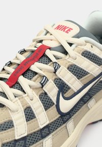 Nike tenisica s bijelim i bež vezicama, plavom mrežastom tkaninom, krem preklopima i crvenim trakicom za povlačenje s natpisom "JUMI BOWMAN SERIES".