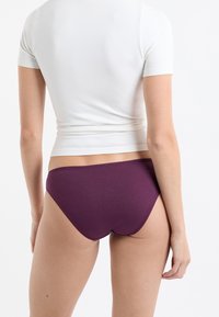 Fioletowe majtki bikini o gładkiej fakturze i niskim stanie, zestawione z dopasowanym białym topem z krótkim rękawem wykonanym z lekkiego materiału.