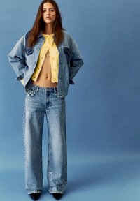 Farmerdzseki széles ujjakkal, alatta sárga, cropped bolyhos pulóver, valamint világos farmere, amely apró hímzett részletekkel és laza fazonnal rendelkezik.