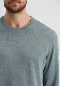 Weicher blaugrüner Pullover mit Rundhalsausschnitt, gerippten Bündchen und glatter Textur. Verfügt über ein minimalistisches Design ohne sichtbare Muster oder Akzente.