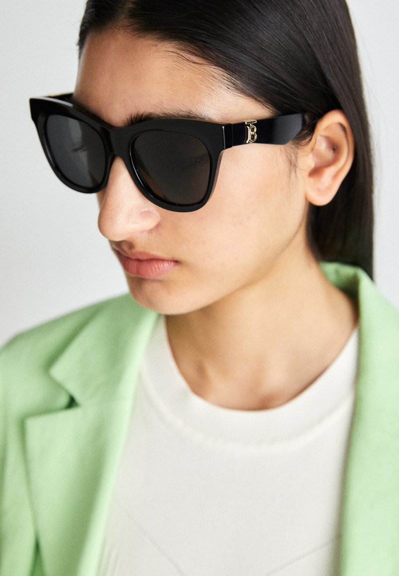 Mustade ülepaisutatud prillid, millel on läikiv viimistlus ja kuldne logo aktsentidel templitel. Kaasas helesinise bleiseriga ja valge ülikonnaga.