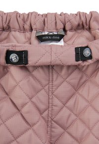 Vatteret pink stof med en blank tekstur, udstyret med en elastisk talje, sorte lynlåsdetaljer og et mærke med brandnavn indeni.