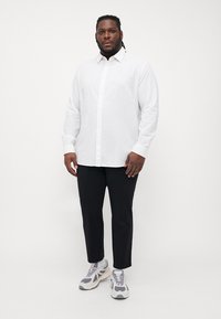 Camicia bianca a maniche lunghe con bottoni, in misto cotone, abbinata a pantaloni neri e sneakers grigie con dettagli bianchi e suola con motivo.