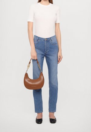 Brun læderhåndtaske med en buet form, kæde i guldaccent, parret med en hvid tætsiddende top, blå jeans og sorte flade sko.