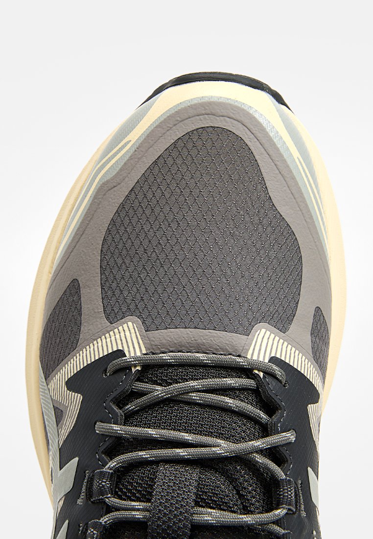 Baskets sportives avec un dessus en mesh gris texturé et des accents noirs, une semelle crème et un motif rayé distinctif sur le côté.