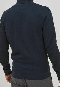 Dunkelblauer gerippter Rollkragenpullover mit langen Ärmeln, der eine figurbetonte Passform und eine einheitliche Textur aufweist. Minimalistisch, ohne sichtbare Muster oder Akzente.
