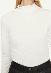 Vit randig långärmad topp med en volangkrage, kombinerad med en svart högmidjad läderskjol, accentuerad av knapprad.