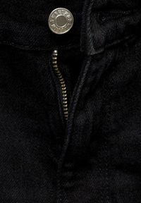 Črn denim jakna v bližnjem posnetku, ki prikazuje srebrno pritrdilno gumb in zlat zadrgo, z teksturirano tkanino in jasnimi detajli šivanja.