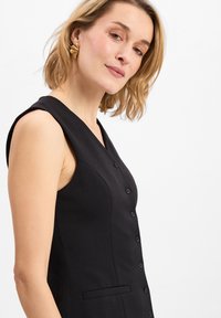 Zwarte mouwloze jurk met een V-halslijn, knoopsluiting en een zijzak. De stof lijkt glad met een gestructureerde pasvorm.