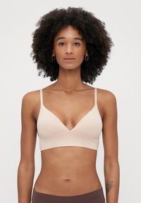 Vaaleanpunainen bralette, jossa on kolmion muotoinen muotoilu, säädettävät hihnat ja sileä kangas, joka ulottuu rinnan alle. Yksinkertainen, saumatonta rakennetta.