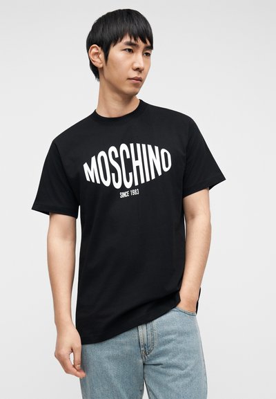 Μαύρο βαμβακερό t-shirt με έντονο λευκό λογότυπο "MOSCHINO" και το κείμενο "since 1983", με άνετη εφαρμογή και κοντά μανίκια. Καθημερινό σχέδιο.