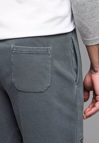 Šedé tepláky mají nášivku na zadní straně, boční kapsy a měkkou texturovanou látku. Elastický pas zajišťuje pohodlné nošení.