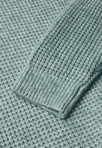 Strickpullover in hellem Aqua mit strukturierter Musterung; verfügt über einen gerippten Bund und gewebte Details für zusätzliche Dimension.