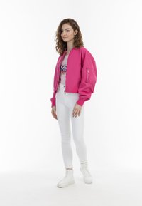 Giacca bomber rosa brillante con tasche con zip, polsini a costine e una vestibilità morbida. Abbinata a jeans skinny bianchi e sneaker bianche.