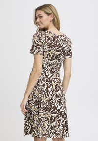 Ruskea kukkakuosisempi mekko lyhyillä hihoilla, pyöreällä kaula-aukolla ja pehmeällä kankaalla. Suunnittelussa on kontrastiväreinä beige ja valkoinen.