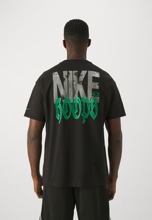 Homme portant un t-shirt noir Nike avec un grand texte gris "NIKE" et un texte vert "HOOPS" dans le dos, debout de dos sur un fond uni.