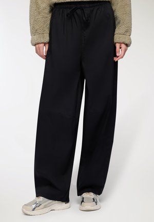 Pantaloni neri, comodi e dal taglio ampio, realizzati in un tessuto leggero e liscio, con una vita elastica regolabile tramite cordino e tasche laterali.
