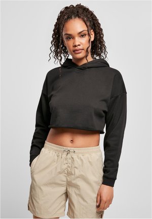 Svart kortstukket hettegenser med lange ermer og snor, parret med lyse beige shorts med elastisk midje. Glatt stofftekstur.