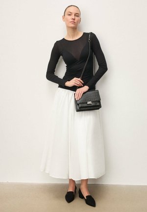 Fekete hosszú ujjú felső áttetsző betéttel, fehér midi szoknya és fekete krokodilmintás kézitáska. A megjelenést fekete hegyes orrú cipők teszik teljessé.