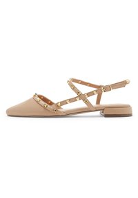 Sandalias planas nude de punta afilada con tachuelas doradas y correas cruzadas en el tobillo. Fabricadas en cuero suave con un tacón bajo.