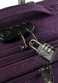 Maleta de tela morada con cremalleras dobles, un candado de combinación negro y una superficie texturizada para mayor durabilidad. Se aprecian detalles metálicos como adornos.