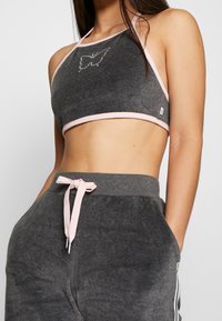 Top corto gris tipo halter con ribete rosa y un diseño de mariposa, combinado con pantalones de chándal grises que cuentan con un cordón rosa y franjas laterales.