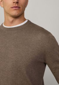 Brązowy sweter dzianinowy z okrągłym dekoltem, charakteryzujący się miękką teksturą i dopasowanym krojem, nałożony na białą koszulę.