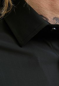 Schwarzes Hemd mit strukturiertem Kragen, glatter Textur und einer einzigen Knopföffnung am Hals.