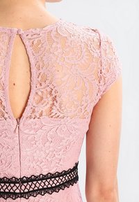 Rosa spetsklänning med korta ärmar, en nyckelhålsrygg och ett svart dekorativt midjeband med intrikata mönster.