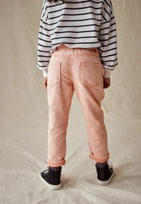 Pantaloni in corduroy rosa con risvolti e tasche posteriori, abbinati a una camicia a maniche lunghe bianca e nera a righe. Sneakers visibili sotto.