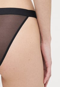 Black mesh thong with a smooth, elastic waist, featuring a sheer fabric and simple, minimalist design. The texture is lightweight.