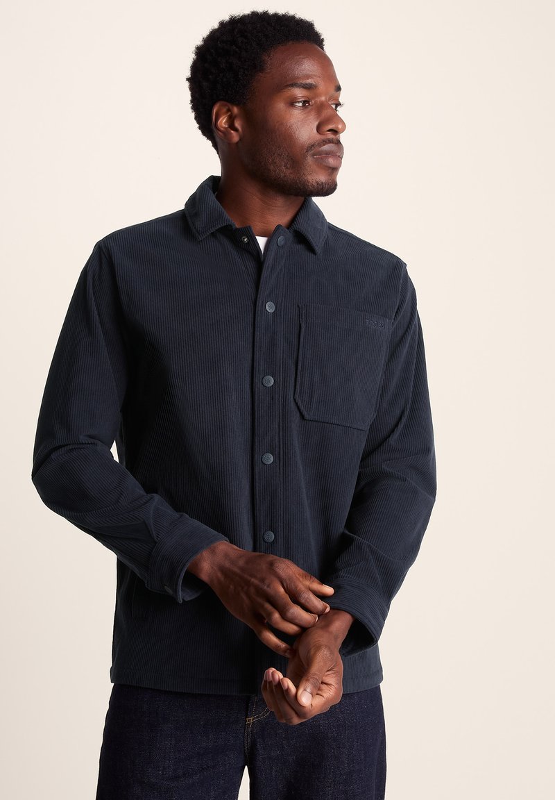Navy corduroy shirt featuring a standard collar, front buttons, a chest pocket, and long sleeves with buttoned cuffs. Textured fabric.