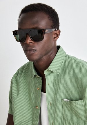 Green striped short-sleeve shirt with a buttoned collar, featuring a chest pocket and a white undershirt. Dark sunglasses with black lenses.