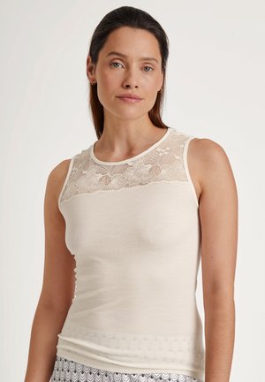 Ärmelloses Oberteil in Creme mit geripptem Stoff, Spitzenakzenten über den Schultern und einem gewellten Saum, der eine taillierte Passform bietet.