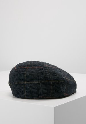 Casquette plate newsboy gris foncé à motif chevrons avec de fines lignes rouges et jaunes discrètes reposant sur une surface blanche.
