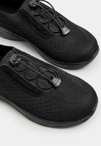 Zwarte sportieve schoenen met een bovenwerk van mesh en suede, elastische veters en een textuurpatroon, met een gevoerde zool voor comfort.