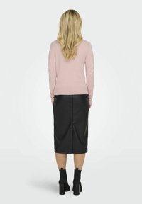 Hellrosa enganierter Pullover kombiniert mit einem schwarzen Leder-Midirock, der einen Schlitz hinten hat, und schwarzen Stiefeln mit Absatz in Knöchelhöhe.