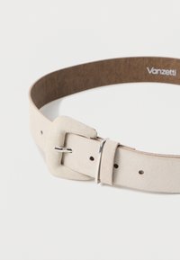 Ζώνη από σουέτ σε ανοιχτό μπεζ χρώμα με υφή, διακοσμημένη με τετράγωνο κούμπωμα και μεταλλικές λεπτομέρειες, συνδεδεμένη με εσωτερική επένδυση από καφέ υλικό.