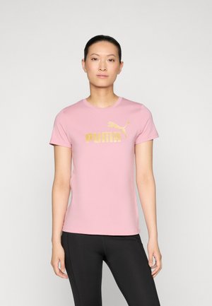 Roosa puuvillane t-särk lühikeste varrukatega, mille esiküljel on kuldne "PUMA" logo. Seljas mustad spordipüksid.