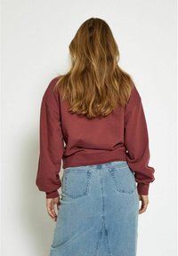 Sudadera marrón con mangas largas, corte relajado y puños acanalados, combinada con una falda de mezclilla de cintura alta y bolsillos traseros.