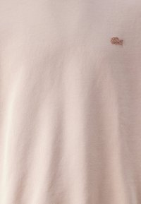 Pulóver de color rosa claro hecho de una tela suave con un pequeño logotipo bordado en el pecho. Textura lisa con cuello acanalado.